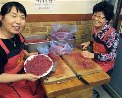 広蔵市場のユッケ専門店「チャメチッ」で仕入れた牛肉を切る金玉姫さん（左）ら＝８日、ソウル（共同）